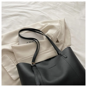 Dettaglio di borsa tote in pelle nera opaca con finiture dorate su blazer bianco