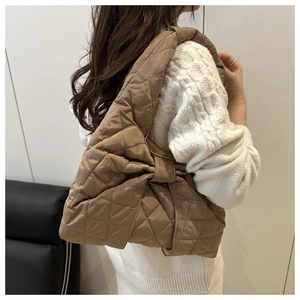 Detailansicht einer braunen gesteppten Tragetasche mit Schleife über einem cremefarbenen Pullover