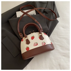 Detailed view of cream and brown strawberry print crossbody bag on a grey blazer