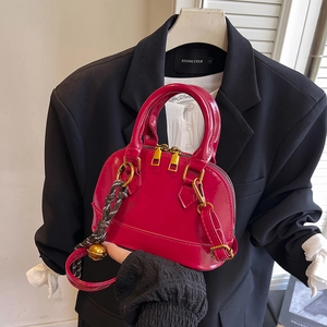 Glossy red shell bag with gold hardware and woven charm shown against a black blazer