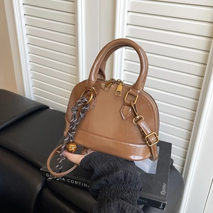 Brown glossy shell-shaped handbag with adjustable strap and decorative bell pendant