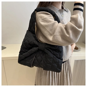 Detail einer schwarzen gesteppten Schultertasche mit glänzendem Stoff und Schleife