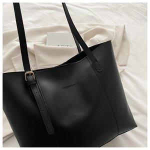 Dettaglio della borsa tote minimalista in pelle nera con logo su un blazer tinta beige