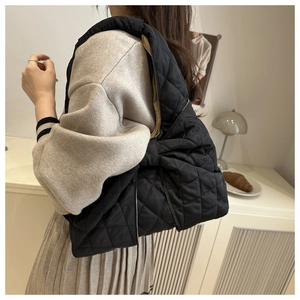 Schicke schwarze Stepptasche mit großer Schleife, getragen von einem Model im Innenraum