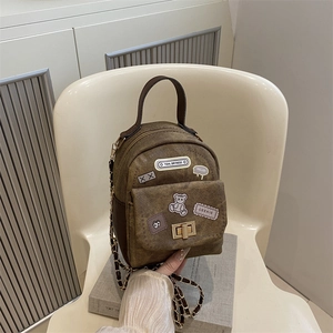 Mini brown fabric backpack with vintage patches and metal chain strap on a white chair