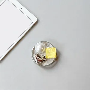 Detail of round phone grip with silver foil texture, white pearl and metal heart decor