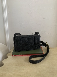 Close-up of black woven square bag with micro-embossed patterns and gold hardware
