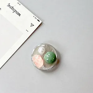 Detail of round phone grip with faux pearl, pink gemstone, and green stone inlay