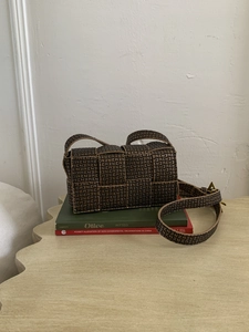 Macro detail of brown woven leather texture with luxury monogram and gold buckle