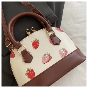 Detail of cream shell bag with red strawberry print and brown leather handles