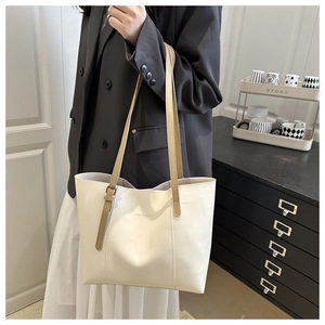 Detail of minimalist cream tote bag showing long brown shoulder straps and side buckles