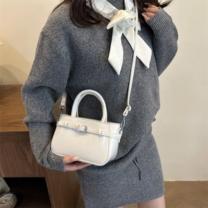 Minimalist white leather bucket bag with top handle and crossbody strap on a model
