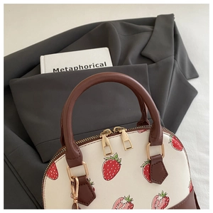 Dettaglio borsa con stampa fragola, doppia cerniera dorata e manici in pelle marrone