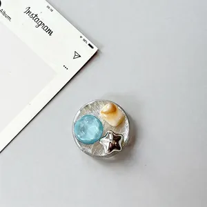 Detail of round phone socket with blue gemstone, marble square and silver star charms