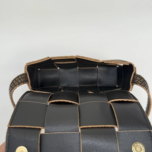 Detail view of woven black leather mini bag with gold magnetic buckle and patterned strap