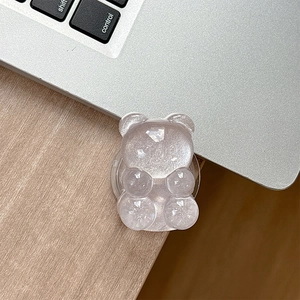 Macro shot of glittery resin bear phone grip on a silver laptop and wood background