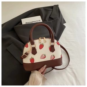 Close-up of shell bag featuring strawberry print, color-block design, and gold hardware