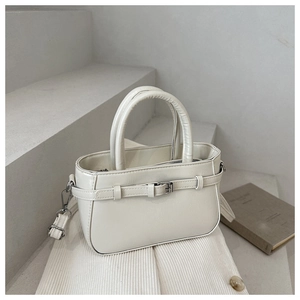 Close-up of minimalist beige PU bucket bag with metallic buckle on stone steps