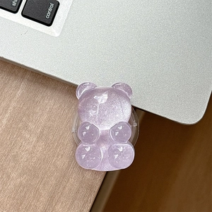 Detail of a purple translucent glitter bear phone grip on a silver laptop surface