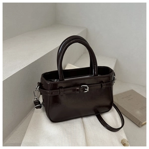 Detail view of a dark coffee patent leather bucket bag with silver buckle and top handle