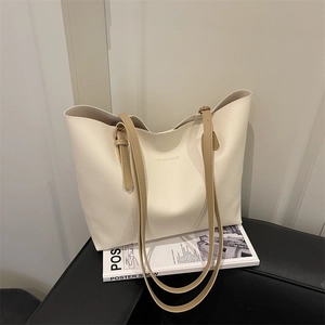 Minimalist off-white leather tote bag with brown straps on a fashion magazine background