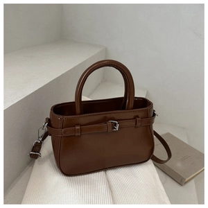 Detailed view of brown PU leather handbag featuring metal buckles on white fabric
