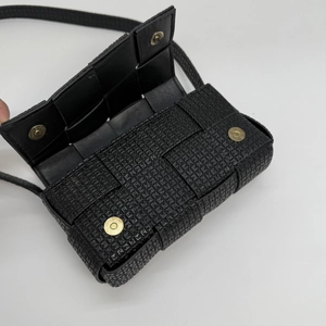 Detail of black woven leather crossbody bag showing dual gold magnetic buckles