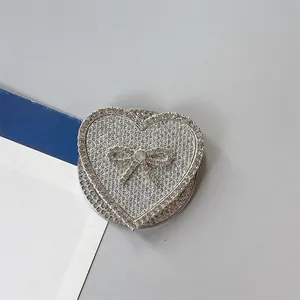 Vista macro del soporte de móvil en forma de corazón con pedrería y un lazo plateado