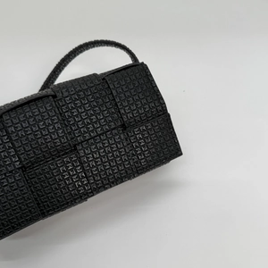 Detail of black woven crossbody bag featuring glossy textured finish and intricate patterns