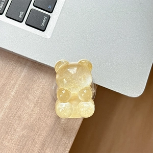 Close-up of translucent yellow gummy bear phone grip on a laptop and desk surface