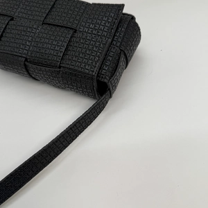 Close-up of wide woven leather texture and shoulder strap detail on a black crossbody bag