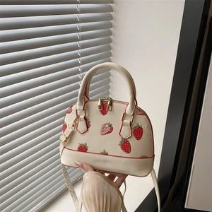 Cream shell bag with red strawberry print, top handles and adjustable strap