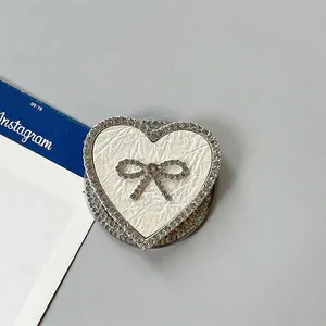 Detalle del soporte de móvil de corazón con textura de cuero crema y lazo de strass