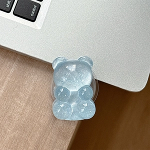 Detail of a light blue translucent glitter bear phone grip on a laptop and wooden desk