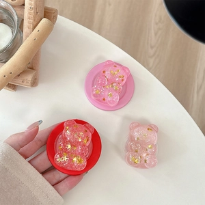 Close-up of three glitter bear phone grips with gold stars on a white table
