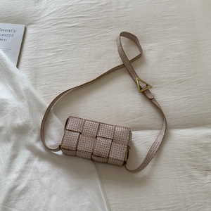 Brown and cream woven crossbody bag with iconic gold triangle buckle on soft white fabric