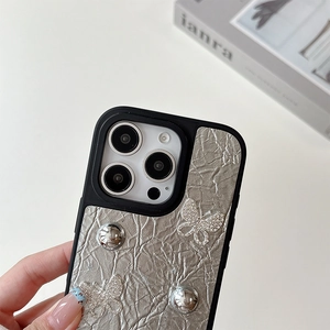 Gros plan d'une coque argentée à texture froissée avec papillons en strass et perles en métal