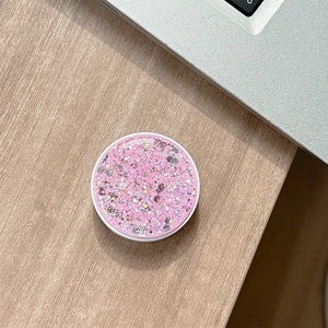 Macro shot of pink glitter phone grip with sequins on a minimalist wooden desktop background