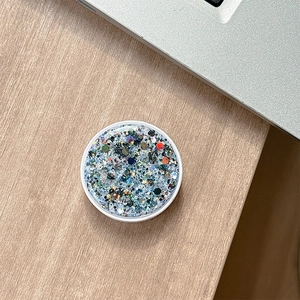 Close-up of a round phone grip with colorful glitter and sequins on a wooden desk