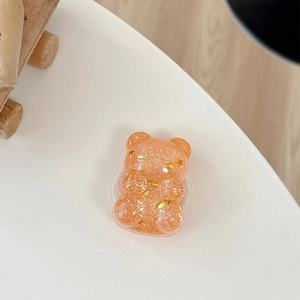 Close-up of glitter bear phone grip with golden stars and orange sequins on white desk