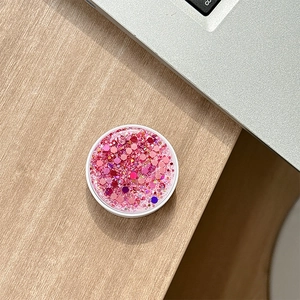 Detailed view of pink glitter sparkle foldable phone grip on a modern wooden desk