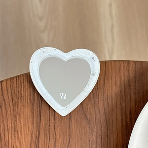 Close-up of heart-shaped glitter mirror with mine logo on a textured wood surface