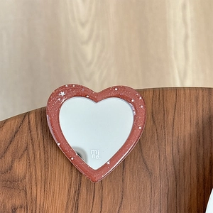 Macro shot of heart-shaped glitter phone mirror bracket with mine logo on wooden surface