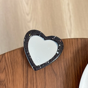 Close-up of heart-shaped glitter phone grip with vanity mirror on a walnut wood table
