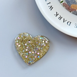 Detail of heart phone grip with golden glitter and laser holographic sequins on blue desk