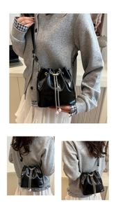 Details einer schwarzen glänzenden Beuteltasche mit Silberkette und Perlen-Kordelzügen