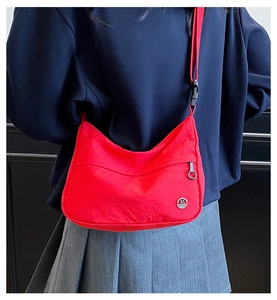 Detail of red nylon shoulder bag featuring metal M logo and adjustable strap on a model