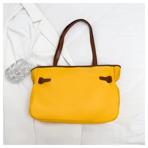 Détail du cabas en nylon jaune avec anses en cuir marron foncé et boucles décoratives