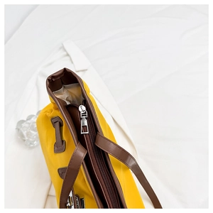 Détail du sac en toile jaune avec anses en cuir marron et fermeture éclair argentée