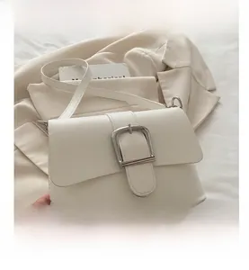 Detail of cream square crossbody bag featuring a large silver horseshoe metal buckle